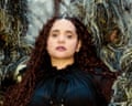 Lido Pimienta stands in a forest, surrounded by strange green woolly faceless figures