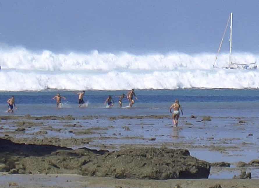 Tourists look far beyond the beach as tsunamis loom behind them.