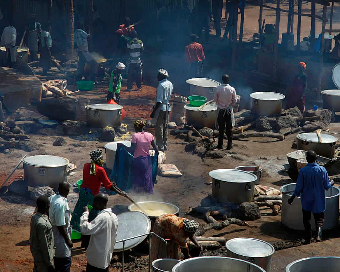 People cook in large metal vats in a Ugandan refugee camp