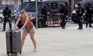 A tourist walks to Barcelona’s cruise terminal as riot policemen keep watch after the protesters.