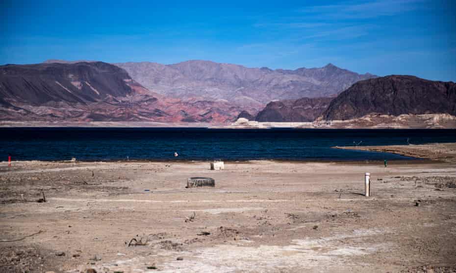 A dry canal path leads to what is left of a lake with mountains in the distance.