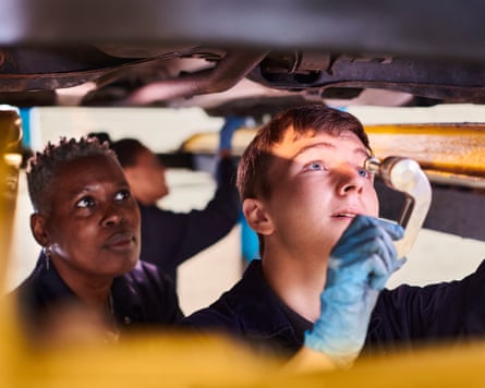 Apprentice mechanic and mentor under a car on a platform