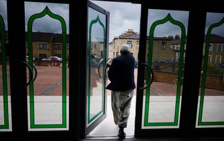 Man exits mosque, photographed from inside, with street outside visible through the glass-panelled doors