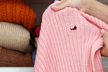 A person holds up a pink sweater with a hole in it