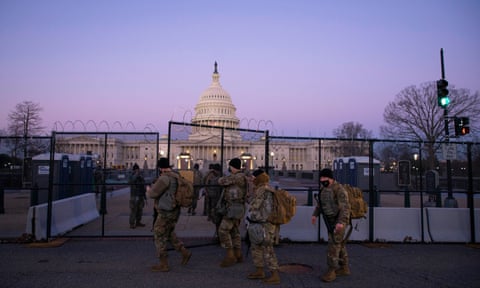 Members of the National Guard enter a gate of barbed wire fencing on US Capitol grounds at sunrise