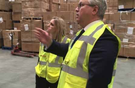 Two people in hi-vis jackets inside a warehouse with lots of cardboard boxes behind them