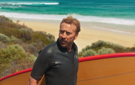 Nicolas Cage carrying a surf board at the beach
