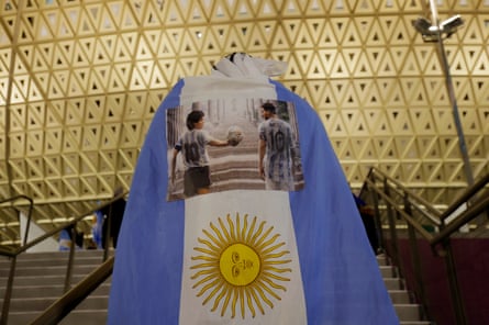 Drums, tattoos and T-shirts: Argentina’s World Cup fan odyssey | Argentina 5 An Argentina fan, draped in a flag bearing the images of Maradona and Messi, walks up the steps to the stadium before the semi-final between Argentina and Croatia at Lusail Stadium.