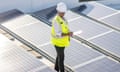 Female African American Solar Engineer<br>African American female inspecting a rooftop of solar panels to ensure efficiency and function while wearing a hard hat and reflective vest.