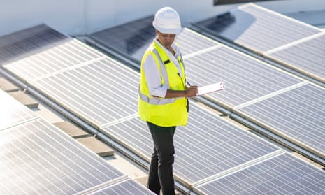 Female African American Solar EngineerAfrican American female inspecting a rooftop of solar panels to ensure efficiency and function while wearing a hard hat and reflective vest.
