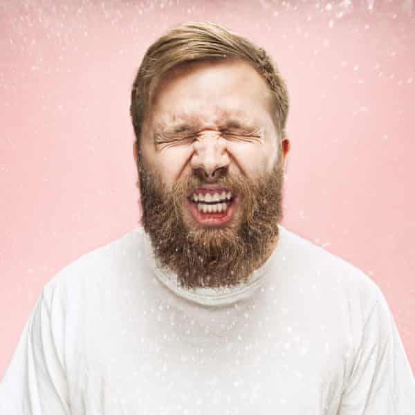 Young handsome man with beard sneezing, studio portrait