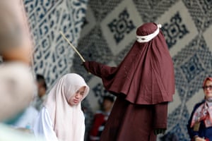 a person in a headscarf hits a woman with a cane