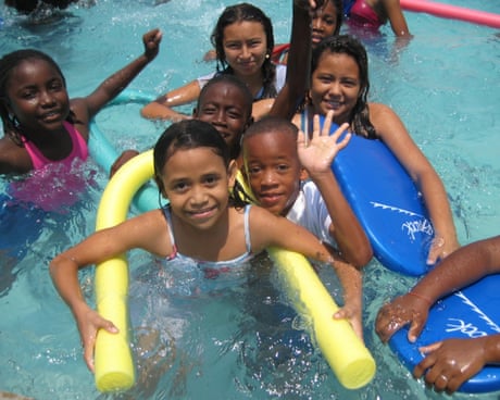 Children in a pool smile and wave at the camera Children in a pool smile and wave at the camera