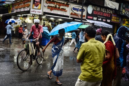 An old woman crosses a road as she protects herself with an umbrella, during the rain, in Chennai