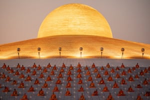 Rows of orange-robed monks sit in front of a golden backdrop