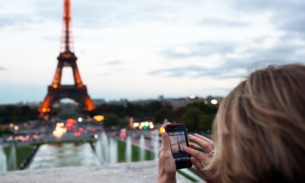 A woman takes a photo of the Eiffel Tower.