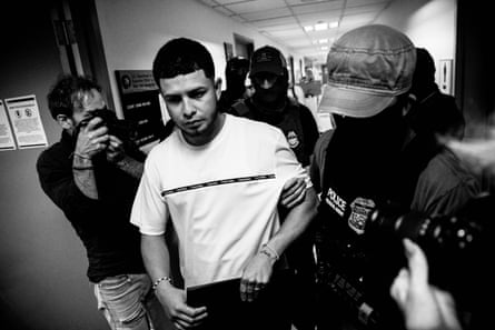 A masked agents holds a man’s arm as they walk to a stairwell