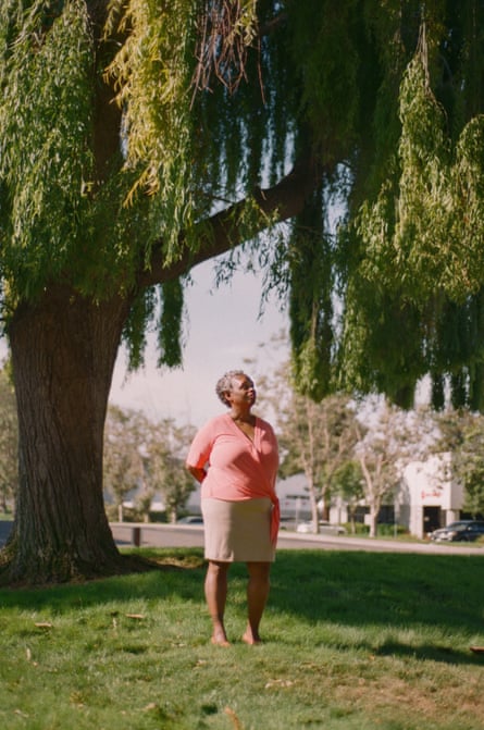 A woman stands beneath the branches of a large willow tree, looking off into the distance.