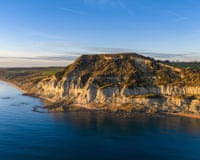 Aerial view of Golden Cap's sunlit cliffs on the Jurassic Coast meeting the sea