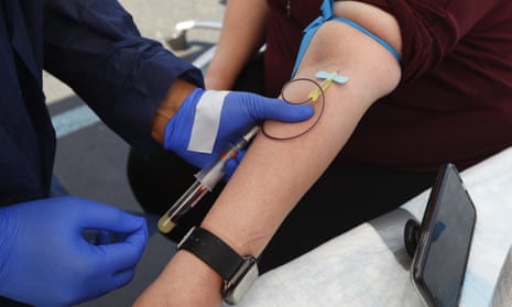 Medic with two gloved hands uses a hypodermic needle to draw blood from someone's arm