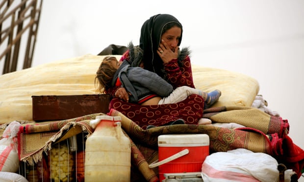 Syrian woman carries her child at a temporary refugee camp