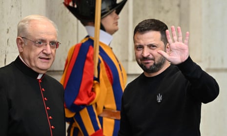 Ukrainian President Volodymyr Zelenskiy waves as he arrives. Standing next to him is the prefect of the pontifical house.