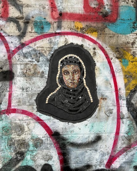 Mosaic design of a woman wearing an Islamic headscarf in a graffitied alley