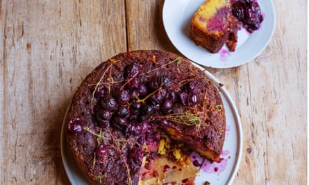 A dark round cake with roasted black grapes on top on a plate with a slice out of it and a side plate with a slice of the cake and roasted grapes on it