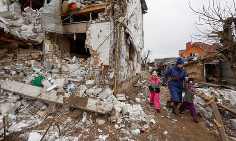 A woman with children walks next to a residential house damaged by a Russian military strike in the town of Hlevakha outside Kyiv.