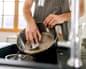 Man uses a scrubber sponge to clean a kitchen pan in sink