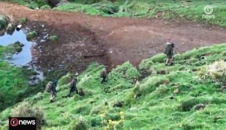 Phillips and his three children hiking across rugged farmland near Marokopa