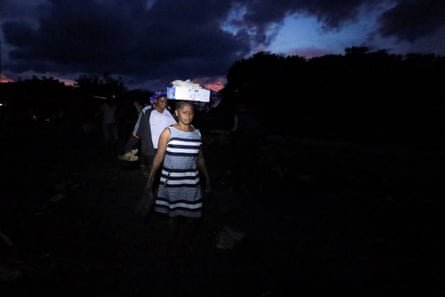 Two women walk in single file in. the darkness, one with a box of possessions balanced on her head.