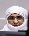 Closeup of al-Hassan sitting in court; he wears glasses and a white headdress wound around his face but his eyes, nose and mouth are visible