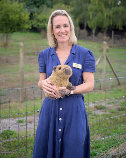 A blond woman in a blue dress holds a toy capybara.