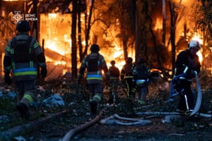 Firefighters walk towards flames. There are long hoses trailed on the ground
