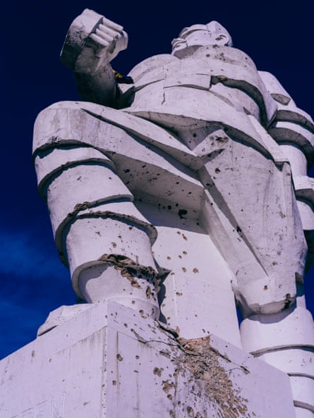 A huge cubist-style Soviet-era statue of a soldier made of concrete and ridded with bullet holes, seen from below