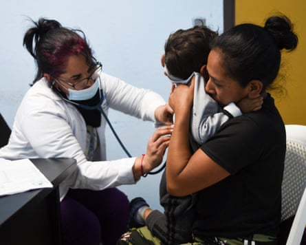 A doctor using a stethoscope to check a child being held up by a woman