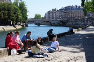 Several people sitting on the ground or on the wall by the river in Paris