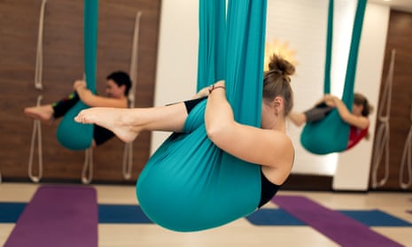 A group of women are hanging in a fetal position in a hammock during an aerial yoga class.