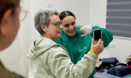 Mandy Damari holds up a mobile phone as Emily Damari raises her bandaged hand while smiling