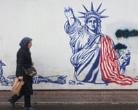Woman in headscarf walks past image of Statue of Liberty with the arm carrying the torch lying on the floor