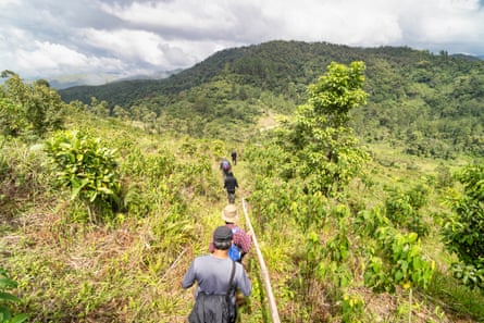 A group of people trek through forested tropical countryside