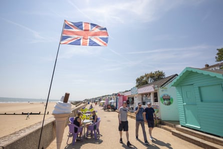 People walking along the seafront at Walton-on-the-Naze with colourful beach huts and a large union flag
