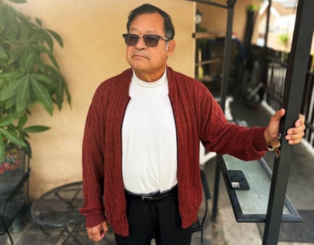 Omar, an older man in sunglasses and a maroon cardigan, stands holding a metal gate