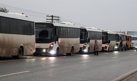 White and grimy buses parked on a roadside as a woman crosses in front