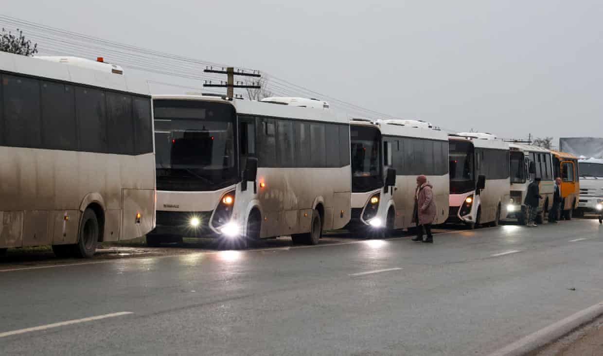 White and grimy buses parked on a roadside as a woman crosses in front