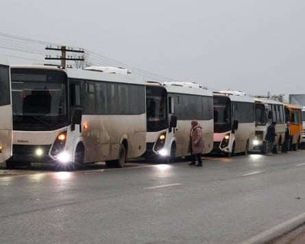 White and grimy buses parked on a roadside as a woman crosses in front
