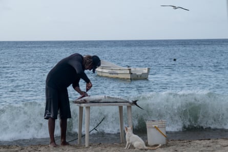 William Álvarez cleans a mackerel on a  small table on the beach