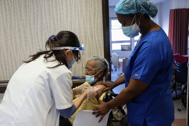 Two medical workers administer care to an elderly woman in a wheelchair.