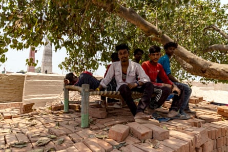 Men sit on a low bench on a pile of bricks under a tree.
